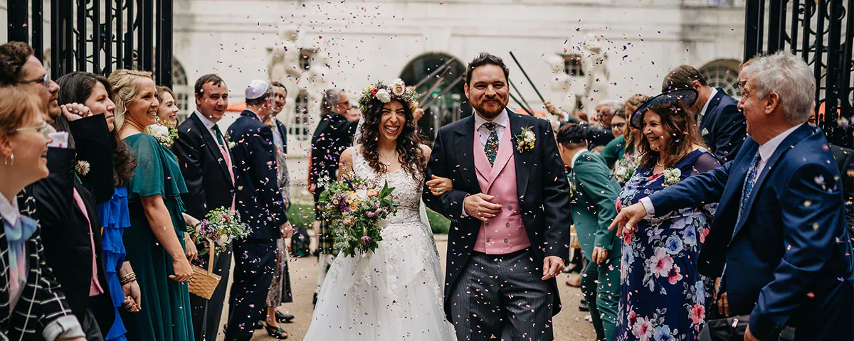 Couple celebrating their wedding day walking out of the venue with their friends and family either side